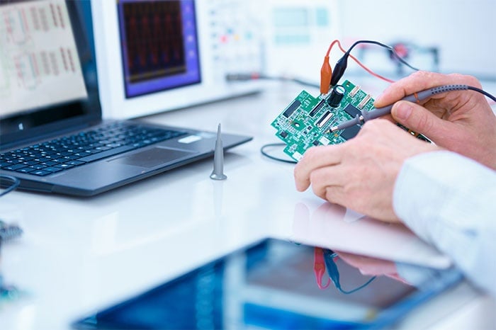 Technician holding a circuit board in front of a laptop