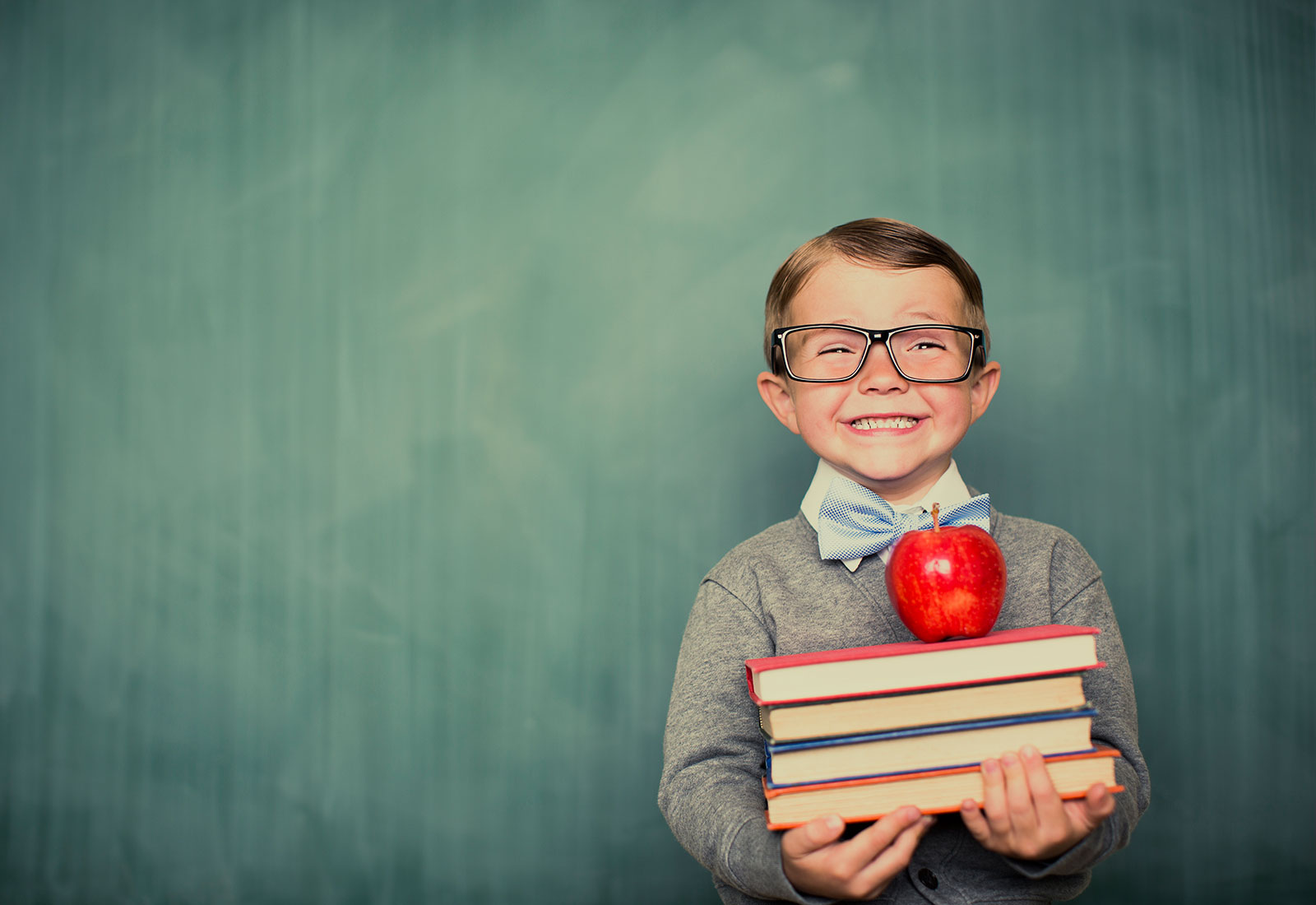 Happy child with glasses holding books and an apple on top
