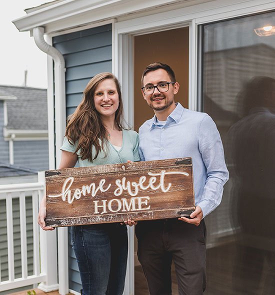 Smiling people holding a wooden board with the inscription "Home sweet home" 